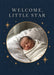 Small ochre stars and sparkles surround an oval photo frame on deep navy, beneath spaced cream serif welcome wording.