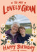 Lovely Gran birthday photo card with cream flowers, green leaves, a peach background and red lettering, shown with a smiling older woman and a boy beside a lake.